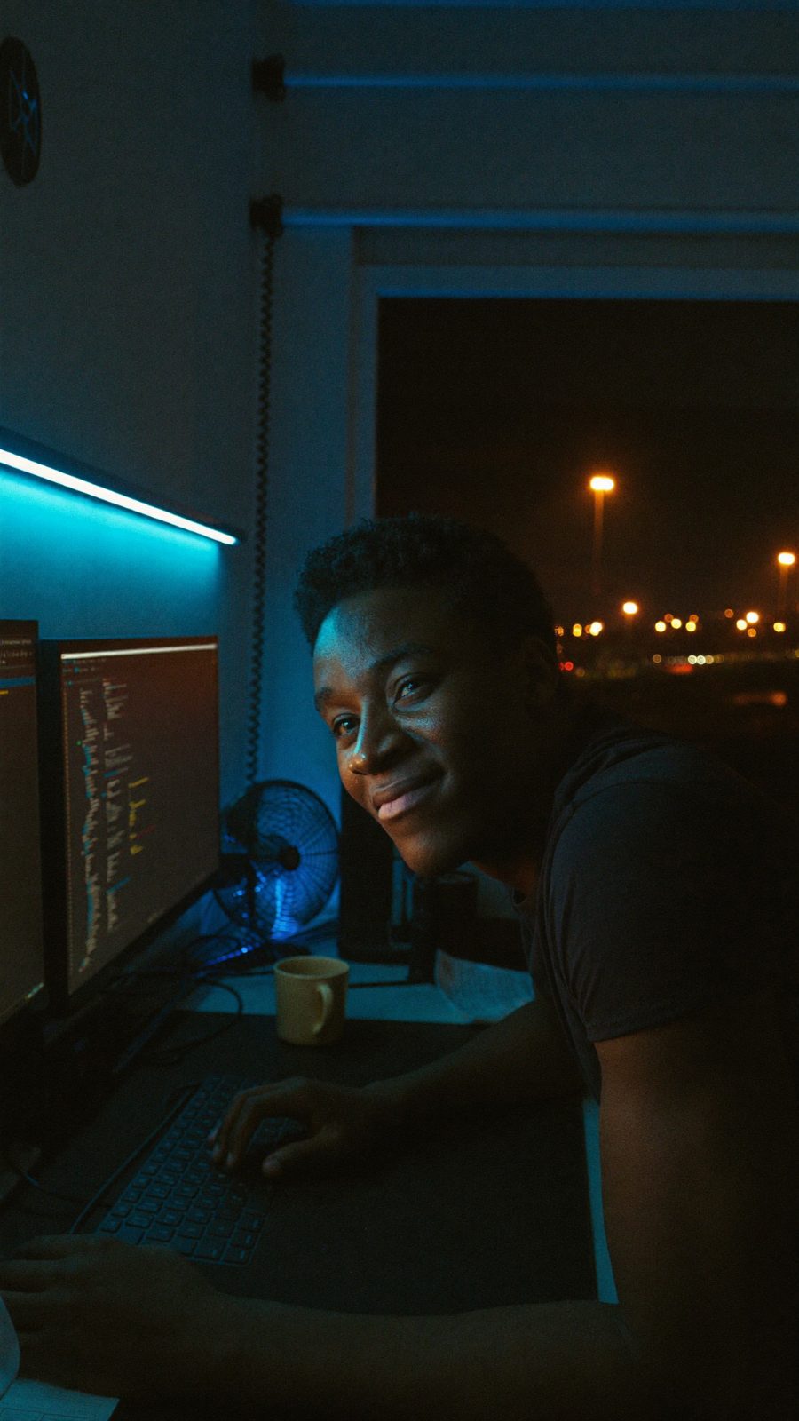 Developer lit by monitor glow and a single blue LED strip in a dark Gweru studio.