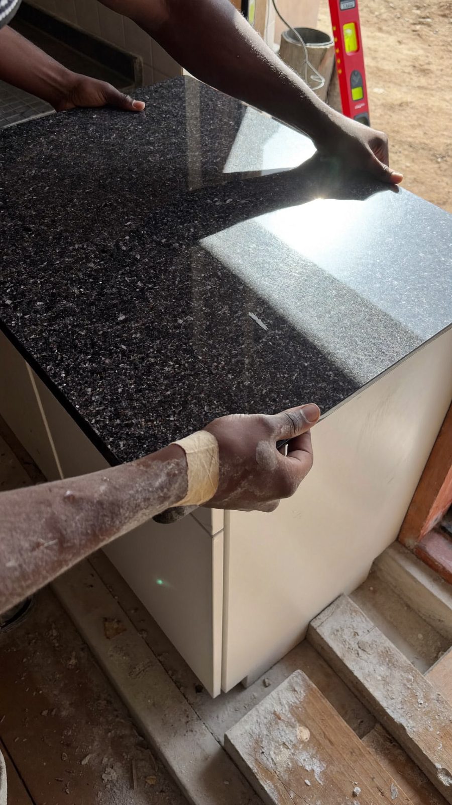Polished black granite slab lowered into a Zimbabwean kitchen in dusty afternoon light.