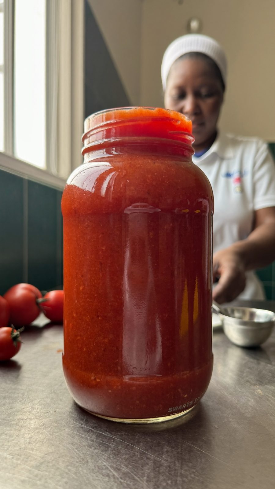 Deep red processed tomato product in glass on an agri-processing floor.