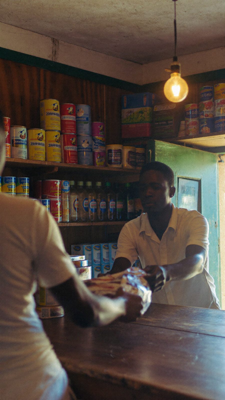 Retail counter interior, goods stacked on shelves, warm tungsten mixed with daylight.